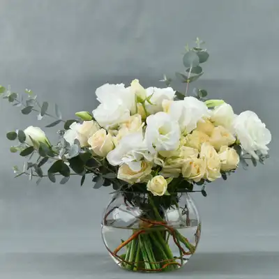 ترتيب أنيق في إناء زجاجي مع زهور الروز الخوخية والليسيانثوس البيضاء